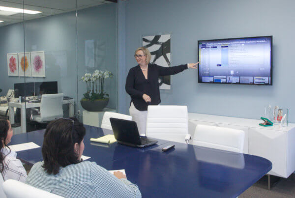 Woman leads a meeting, presenting with a screen on the wall.